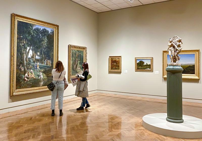 Two women wearing face coverings admire a painting in a large hall at the Minneapolis Institute of Art