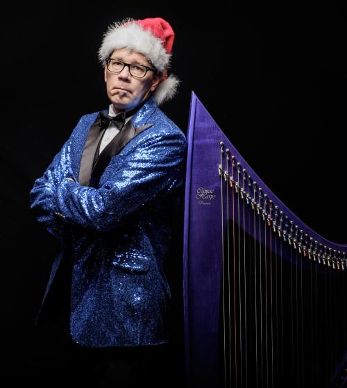 Man in blue suit in a santa hat standing with back against a harp