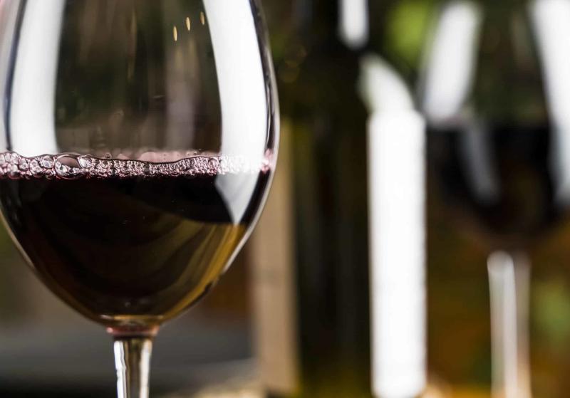 Wine tasting. A glass of red wine on the background of a restaurant table with bottle at an evening dinner or event party.