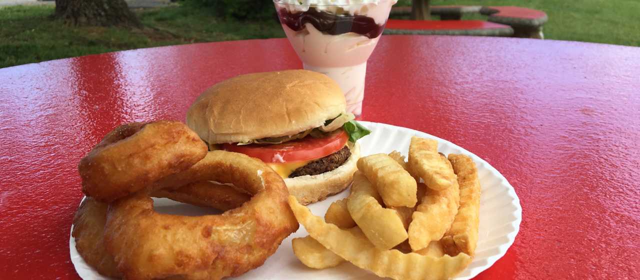A local joint serves up a cheeseburger with onion rings & crinkle-cut fries and an ice cream sundae.}