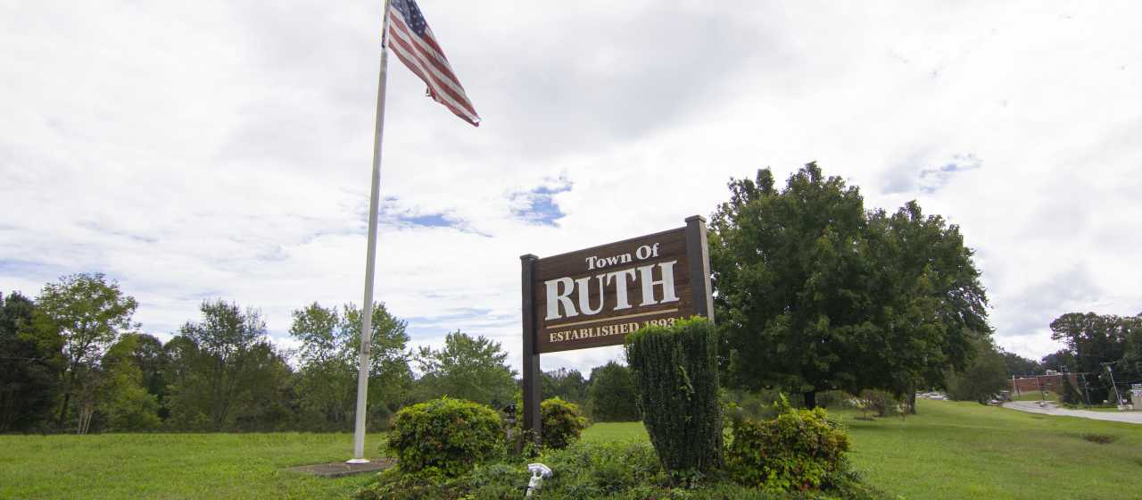 The welcome sign for Ruth, NC on a manicured green park with an American flag.}