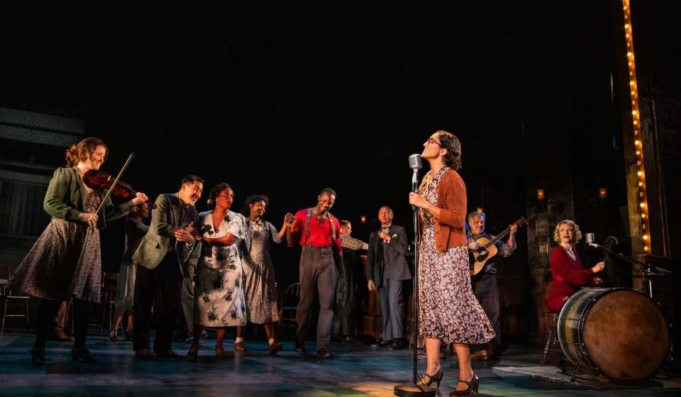 A woman on stage sings as a line of people dance