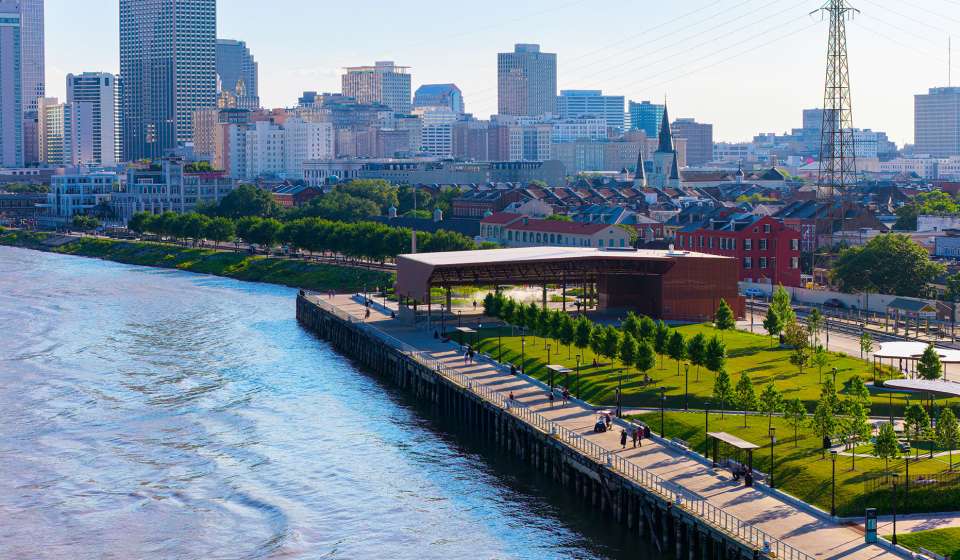 A drone shot of the French Quarter and New Orleans city skyline taken from over the MIssissippi River of the Goldring Woldenberg Riverfront Park at sunset.