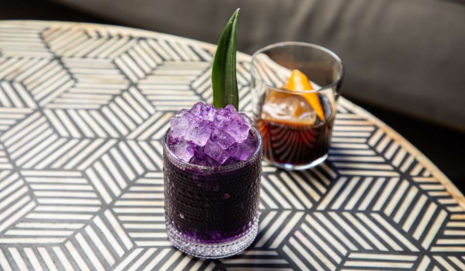 two cocktails, one purple, one brown, on a table