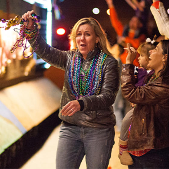 Woman celebrating at a Mardi Gras parade in a crowd, holding Mardi Gras beads