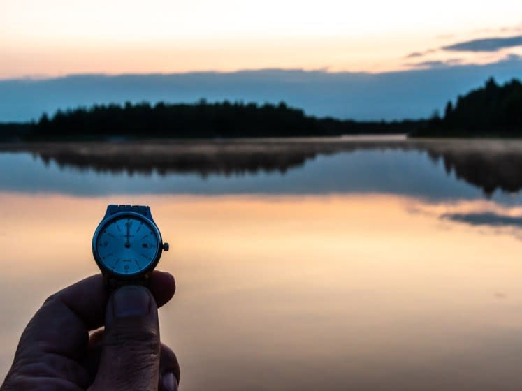 Midnight in Fairbanks - a hand holding a watch face with a view of the sun reflected on a lake