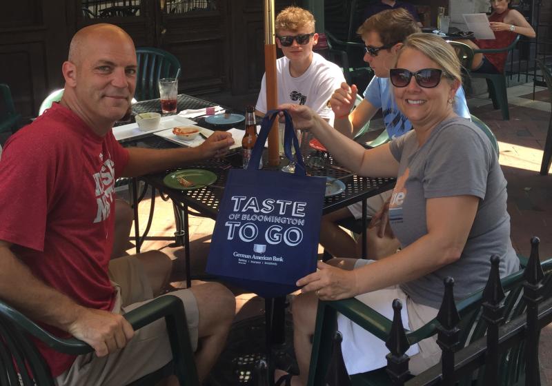 Family sitting at a patio table holding a Taste To Go bag