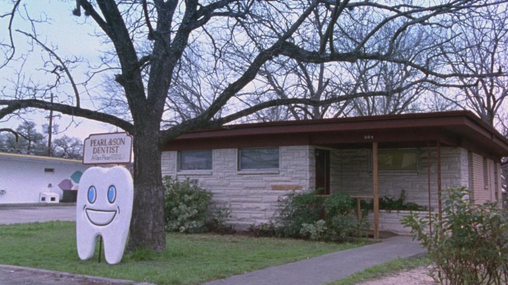 Waiting for Guffman screengrab, showing the Pearl & Son Dentist building and a sign shaped like a smiling tooth in Lockhart Texas