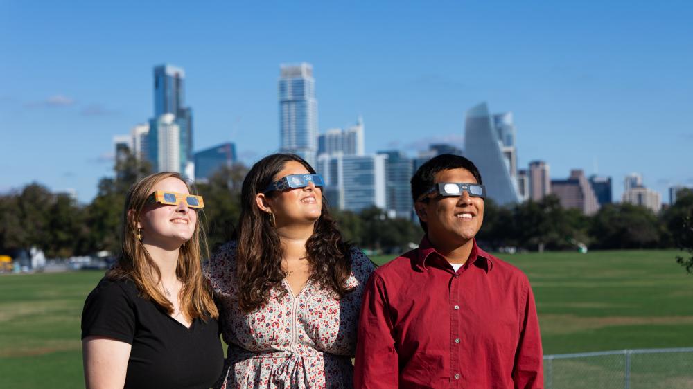 Three people looking at the sun wearing eclipse glasses in Zilker Park.