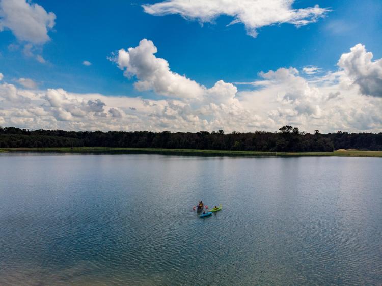 A drone shot of 3 colorful kayaks in a lake with a blue sky.