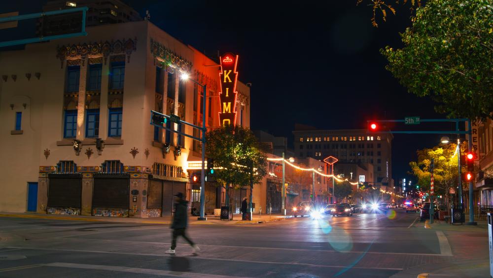Nighttime view of the KiMo Theatre from Central Avenue, with a pedestrian crossing the street.
