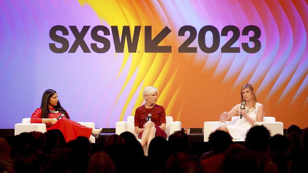 Three women sitting on a stage in a panel discussion, in front of a colorful SXSW 2023 backdrop.