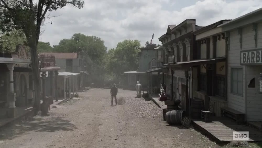 Fear the Walking Dead screengrab showing a western town set as Humbug's Gulch. A man stands in the center of the dusty street with a tumbleweed near his right foot