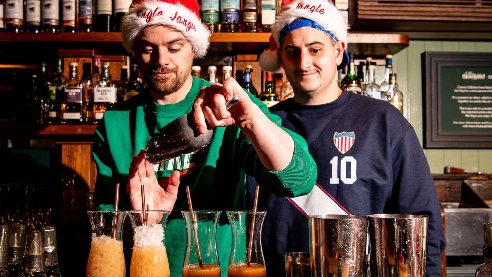 Two bartenders wearing Santa hats, mixing up holiday cocktails.