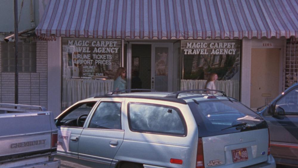 Waiting for Guffman screengrab showing cars parked in front of an office with signs reading Magic Carpet Travel Agency