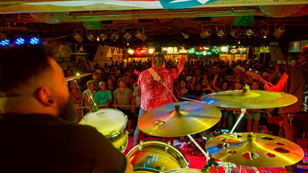 The band Kin Faux playing a show at Gruene Hall with people standing in the crowd in the background.