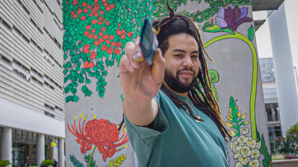 Rex Hamilton holds paintbrush to camera in front of his mural at Seaholm Power Plant in Austin Texas