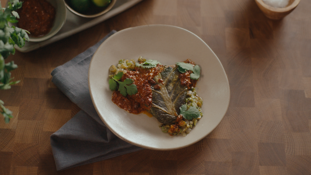 White plate, sitting on a blue napkin topped with a large leaf overflowing with corn and diced vegetables and a sweet potato "chili".