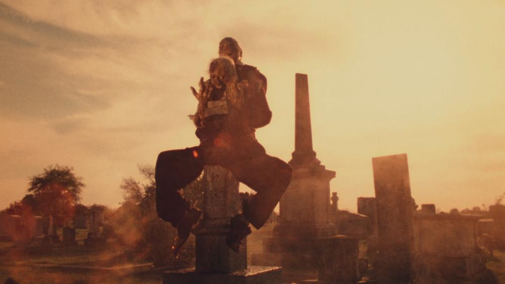 Texas Chainsaw Massacre screengrab showing desecrated corpses mounted on a tombstone in a cemetery in yellow light