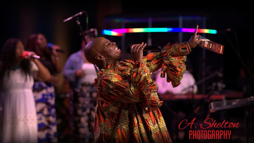 woman singing into a microphone on a stage of singers during a worship service