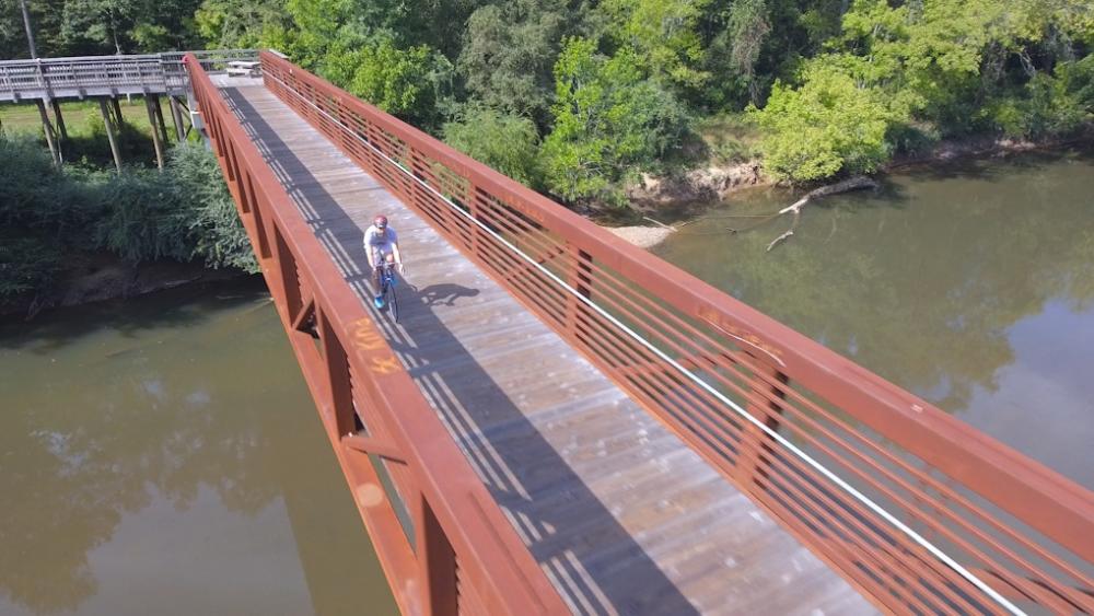 Drone Shot of Man Cycling on a Bridge Over a River