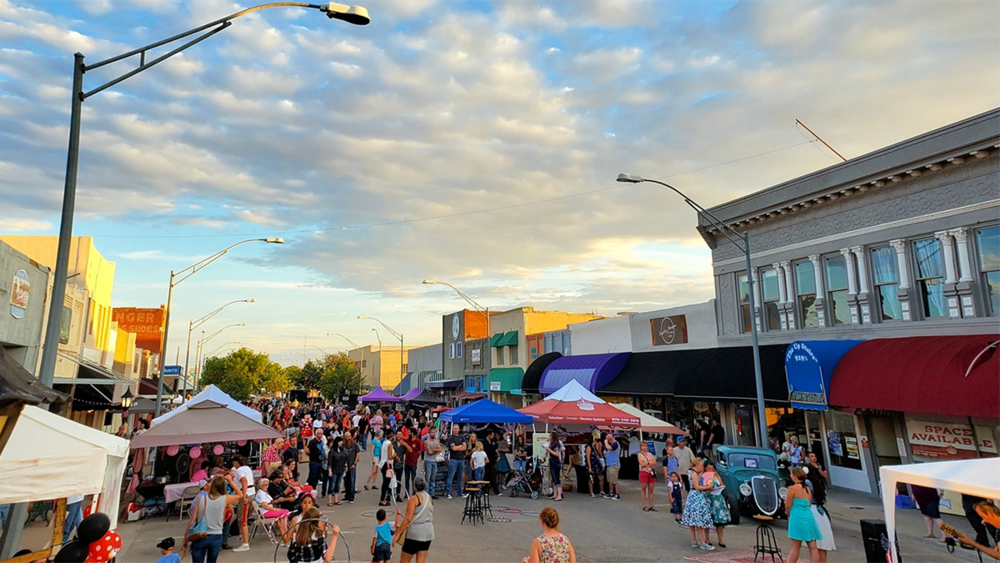 an outdoor market on a town street, with tents and a large group of people milling about