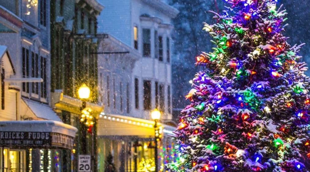 A Christmas tree with colored lights in the middle of Mackinac Island’s Main Street on a snowy winter night with glowing streetlights