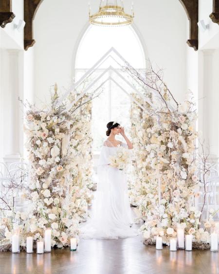 A bride stands in front of a floral arch.