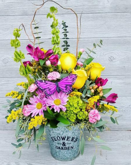 A rose, daisy and carnation flower bouquet in a metal bucket.