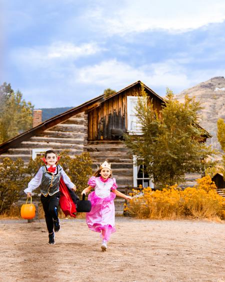 A child dressed as a vampire in a red cape runs alongside another dressed as a pink princess through Golden History Park during the fall Halloween season.