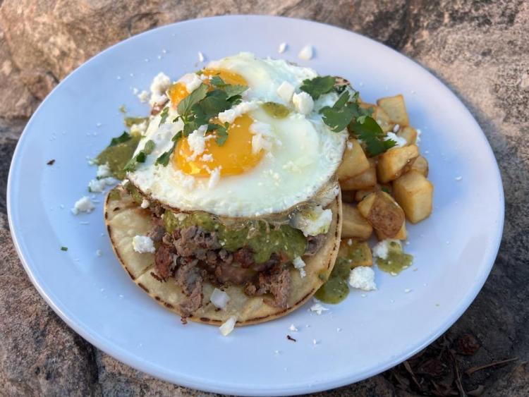 Steak Huevos Mexicanos With Fried corn tortillas, refried beans, thin sliced sirloin topped with salsa verde, 2 eggs, queso fresco, cilantro, and onions served with papas