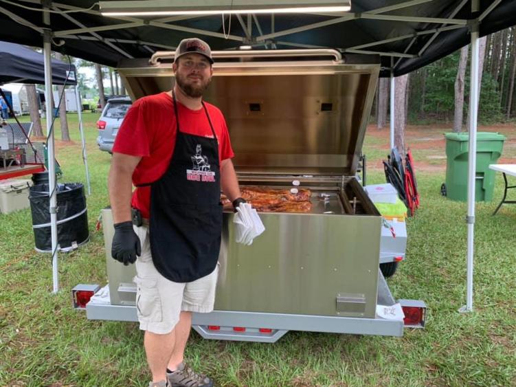 Kevin poses in front of a grill, cooking at a North Carolina BBQ Competition
