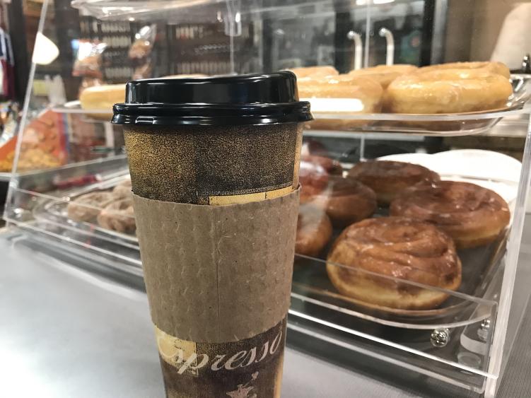 A to-go coffee cup sits in front of a baked goods case