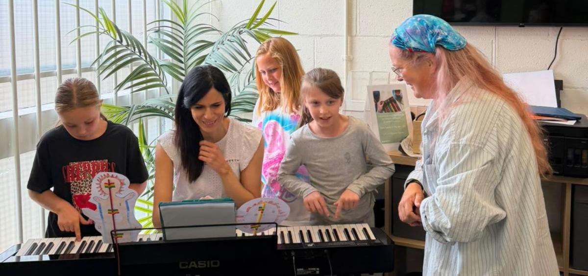 A musician sits at a piano at the reel creative workshop with kids around her