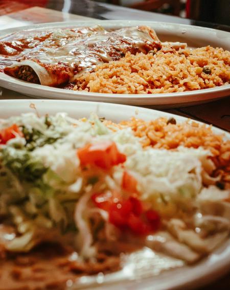 Burrito and Enchilada with rice, lettuce, tomatoes, and beans on a plate
