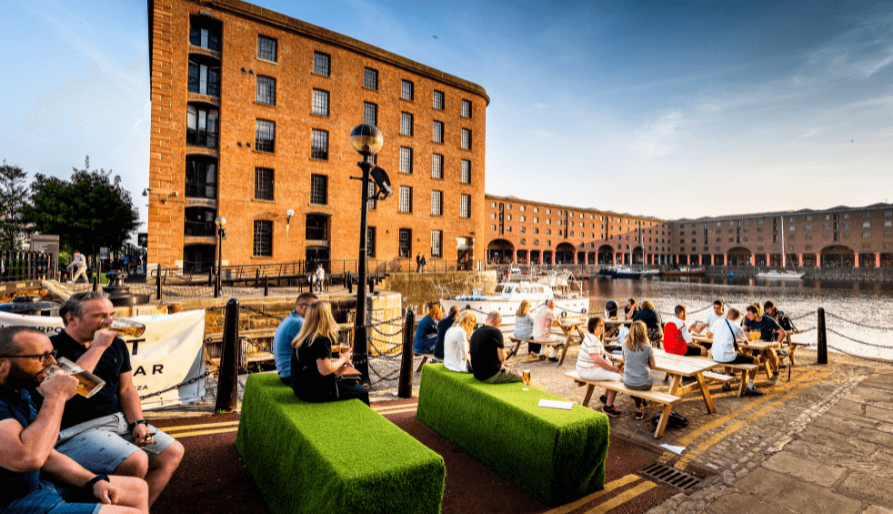 The royal albert dock with people sitting on benches in an outdoor bar.