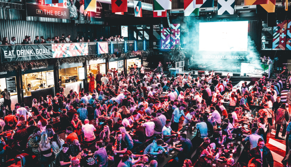 Inside a large warehouse bar with people sitting on long benches.