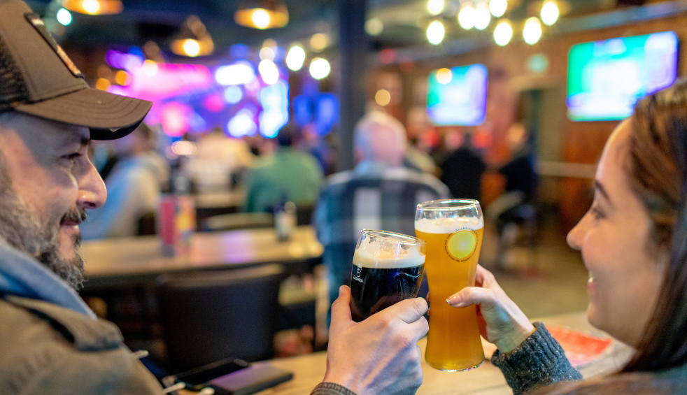 Two people holding drinks and beers together in a 'cheers' position in a bar.