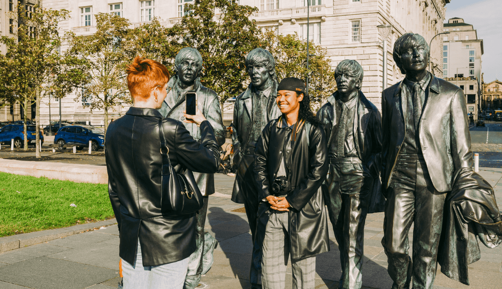 Two people getting their photo taken in front of a large beatles statue