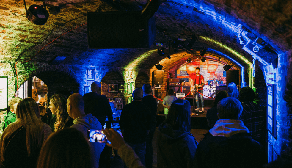 Inside The Cavern Club with a crowd of people watching someone on a stage.
