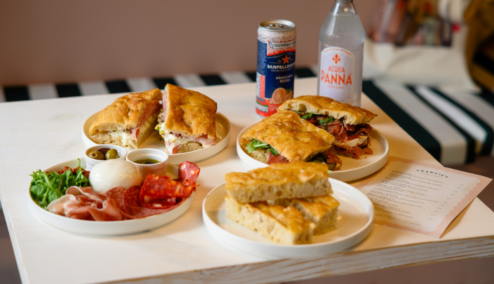 A table with four plates of food on which are sandwiches, salads and bread.