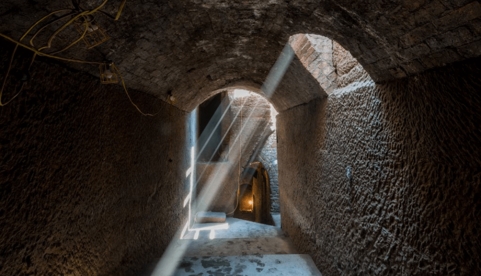 Inside a dark underground tunnels with beams of light shining through windows.