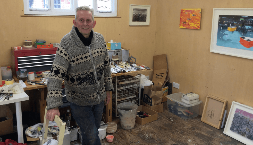 A person stood inside an art studio with paintings on the walls.