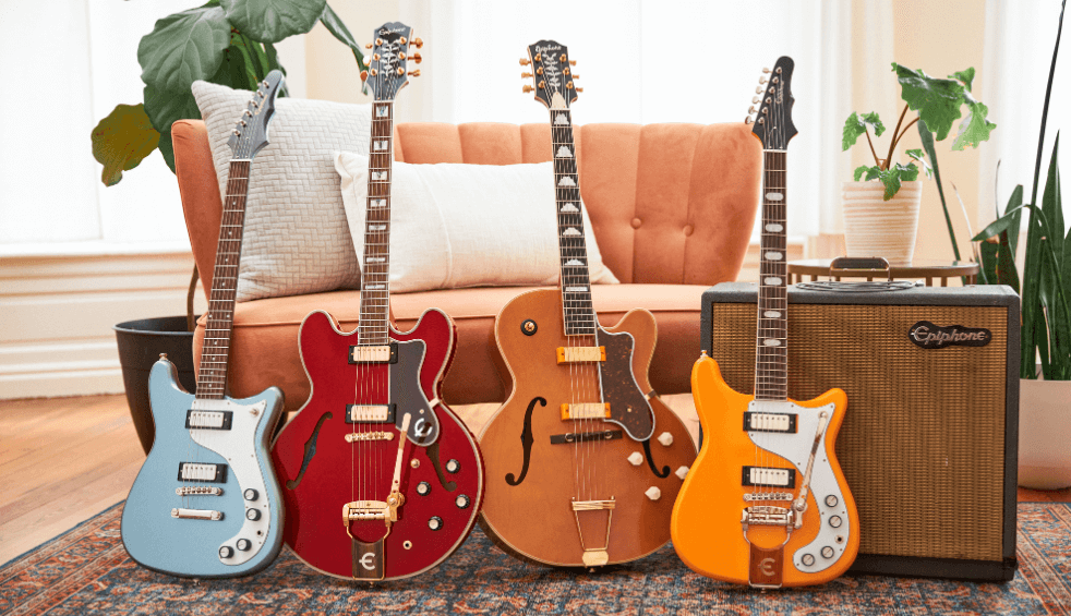 Four guitars lined up in a row next to an amp with a chair behind them.