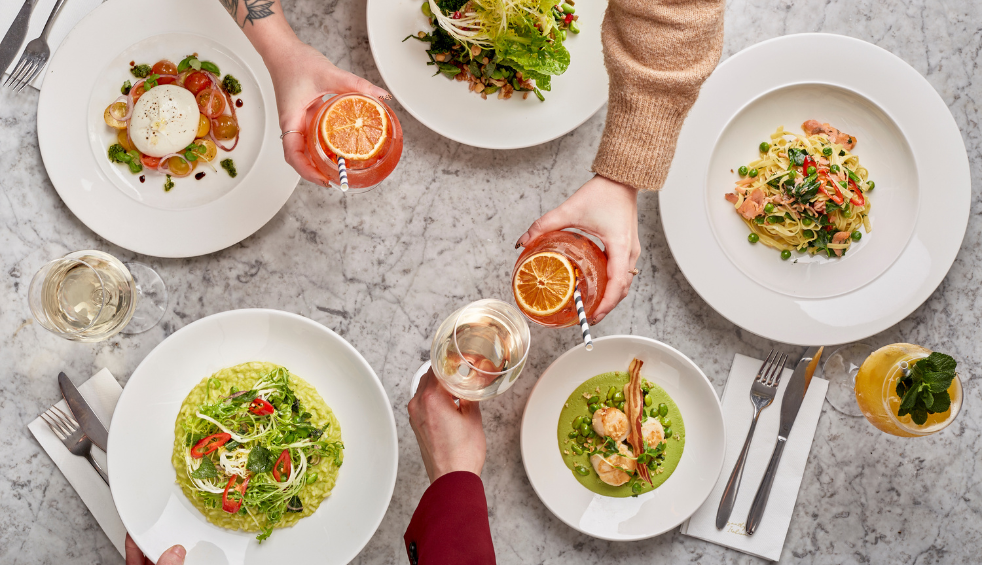 five plates with different dishes on of pasta, salad and people holding drinks.