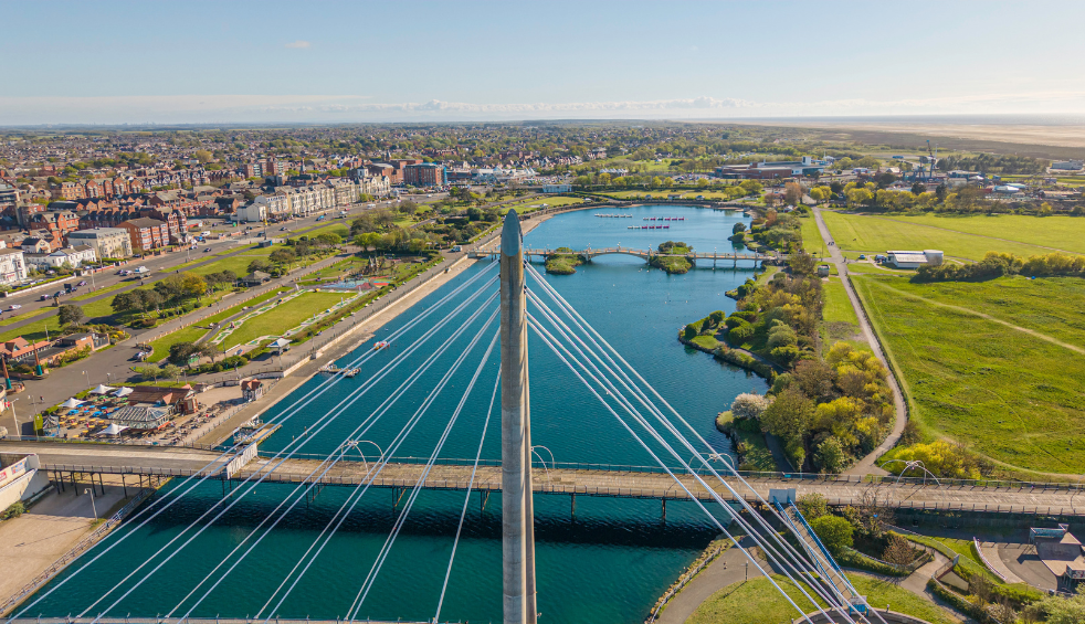 A drone shot of Southport Marine Lake with a bridge going across it. There are green fields to the right.