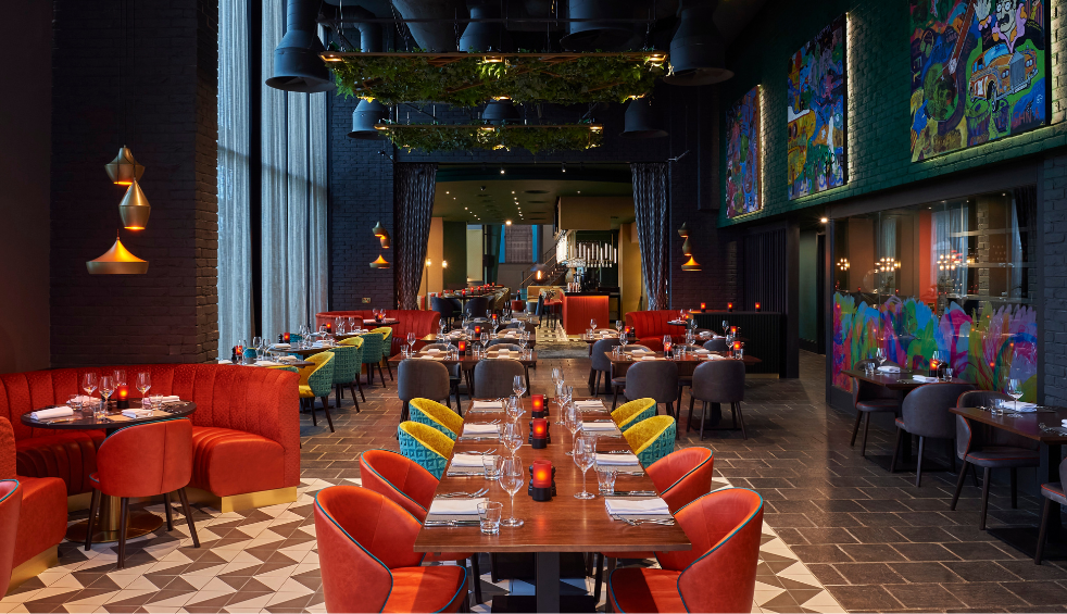 Inside the restaurant at Malmaison with round and long tables with orange chairs.