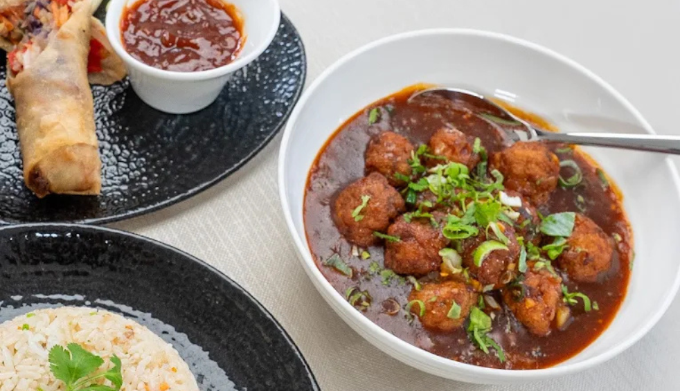 Three plates of food, one with a curry on it, on with spring roles and another white rice.