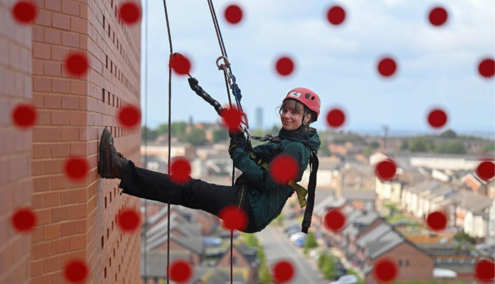 A person doing the Anfield abseil, walking down the side of the building. The glass has red dots on it looking out towards the street.