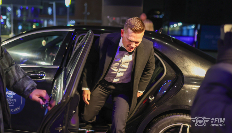 A person stepping out of a black car, wearing a black dinner suit.